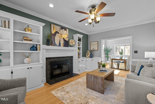 living area with light wood-type flooring, a glass covered fireplace, and crown molding