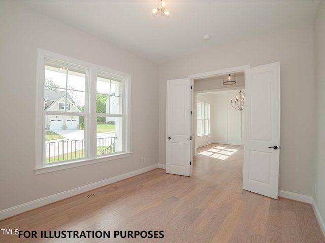 empty room featuring light wood-style floors, visible vents, baseboards, and an inviting chandelier