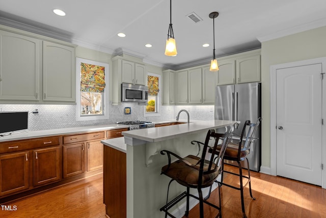 kitchen featuring stainless steel appliances, a kitchen bar, light hardwood / wood-style flooring, hanging light fixtures, and a center island with sink