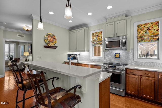 kitchen featuring stainless steel appliances, decorative light fixtures, ornamental molding, tasteful backsplash, and a breakfast bar area