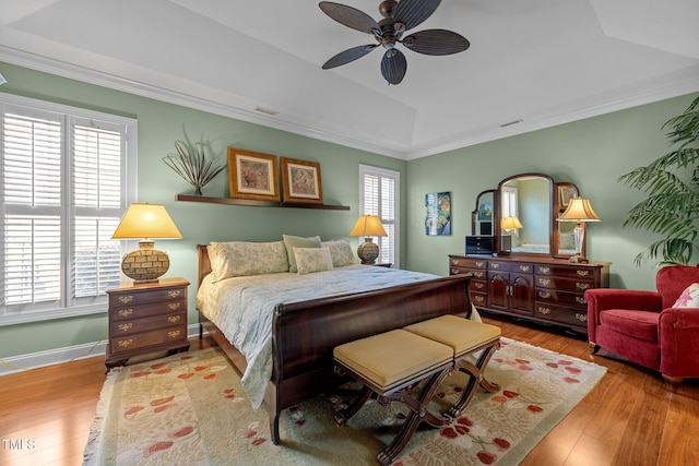 bedroom featuring ceiling fan, light hardwood / wood-style flooring, ornamental molding, and a raised ceiling