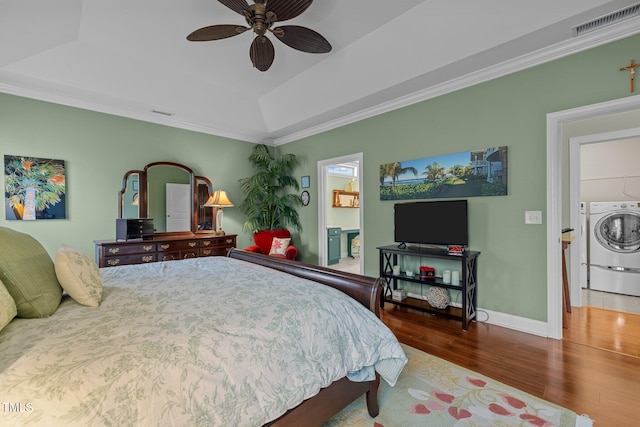 bedroom with hardwood / wood-style flooring, a raised ceiling, connected bathroom, washer / clothes dryer, and ceiling fan