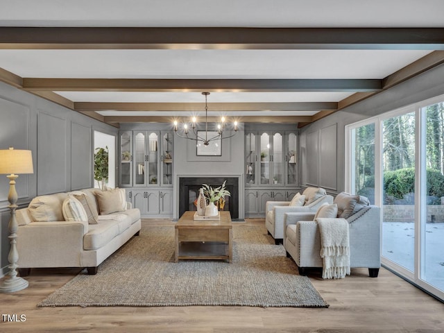 living room featuring beamed ceiling, an inviting chandelier, and light wood-type flooring