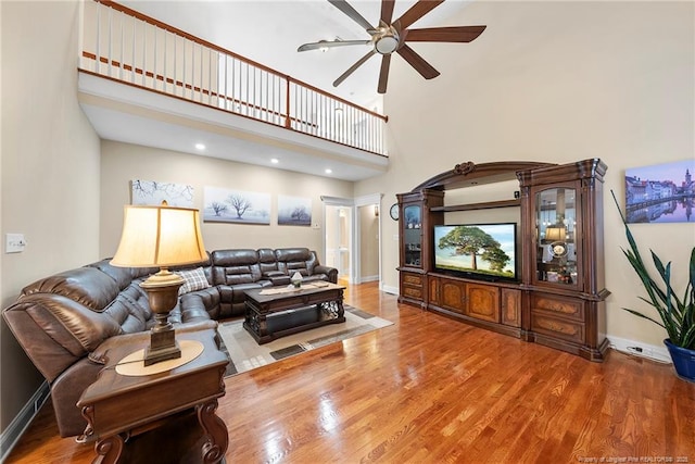 living room with a towering ceiling, hardwood / wood-style flooring, and ceiling fan