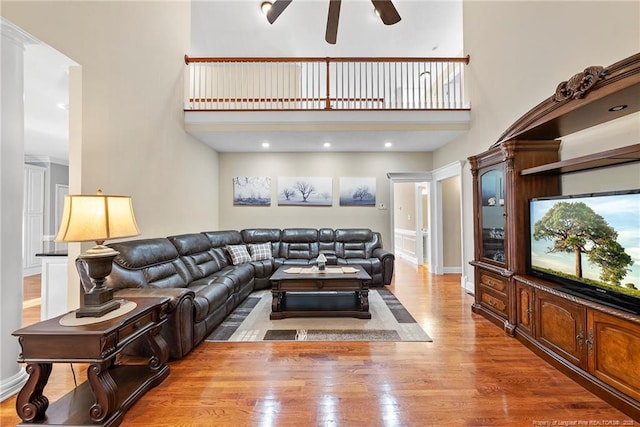 living room featuring ceiling fan, a high ceiling, and light hardwood / wood-style flooring