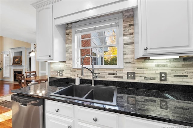 kitchen with stainless steel dishwasher, dark stone countertops, white cabinets, and sink