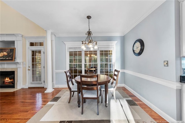 dining space with decorative columns, a tile fireplace, wood-type flooring, and an inviting chandelier