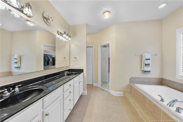 bathroom featuring tile patterned flooring, vanity, and tiled bath