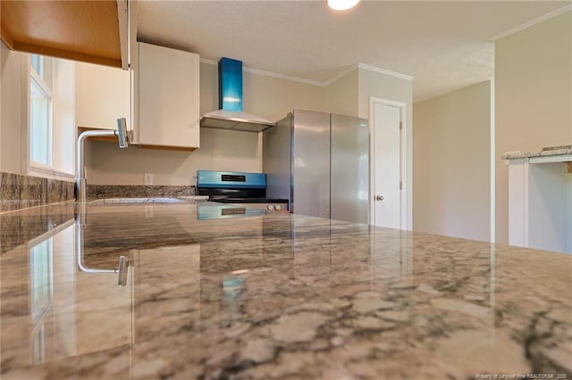 kitchen with stainless steel fridge, stove, wall chimney exhaust hood, sink, and stone countertops