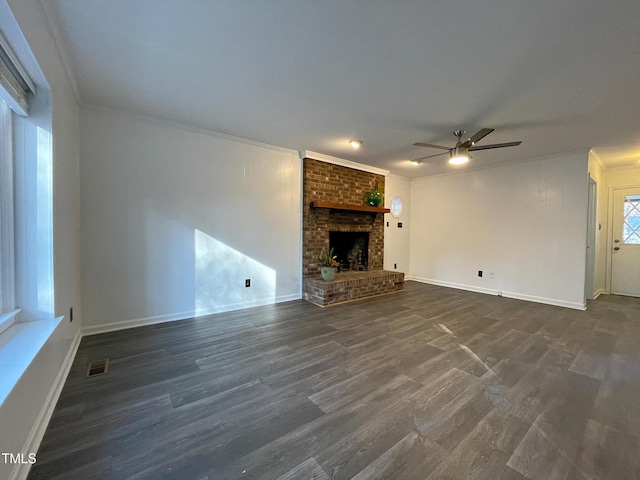 unfurnished living room with a brick fireplace, dark wood-type flooring, ornamental molding, and ceiling fan