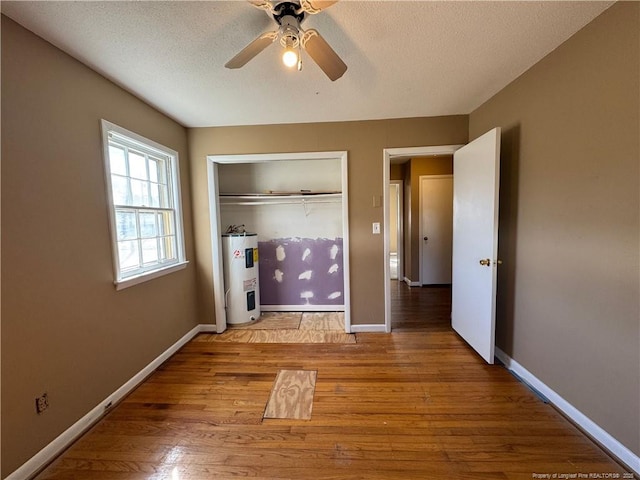 unfurnished bedroom with a closet, light hardwood / wood-style flooring, electric water heater, and a textured ceiling