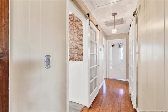 hall with a barn door, wood-type flooring, and wooden walls