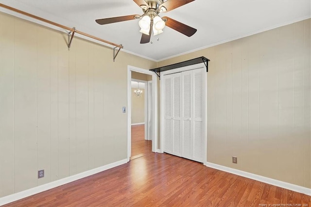 unfurnished bedroom with hardwood / wood-style floors, ceiling fan with notable chandelier, crown molding, and a closet