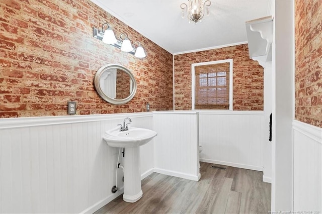 bathroom featuring ornamental molding, brick wall, and hardwood / wood-style flooring