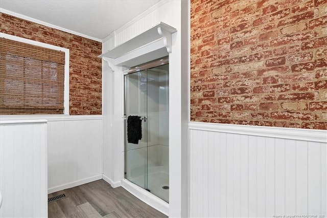 bathroom with wood-type flooring, crown molding, and brick wall