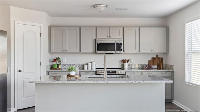 kitchen with gray cabinets, light stone countertops, a center island with sink, and dark hardwood / wood-style flooring