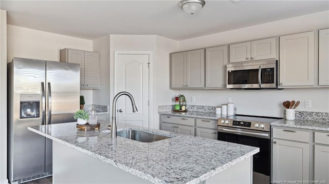 kitchen featuring light stone countertops, gray cabinetry, stainless steel appliances, a kitchen island with sink, and sink