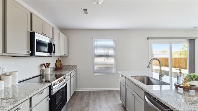 kitchen featuring sink, light stone counters, gray cabinets, appliances with stainless steel finishes, and light wood-type flooring