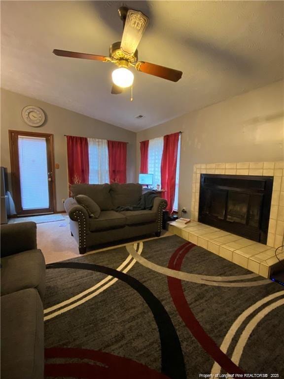 carpeted living room with ceiling fan, lofted ceiling, and a tile fireplace