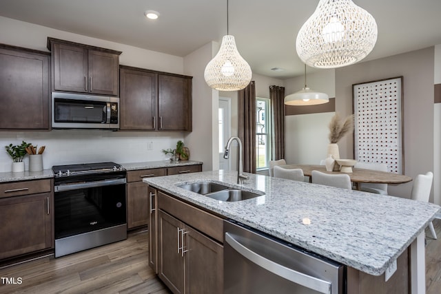 kitchen with pendant lighting, hardwood / wood-style floors, a center island with sink, sink, and appliances with stainless steel finishes