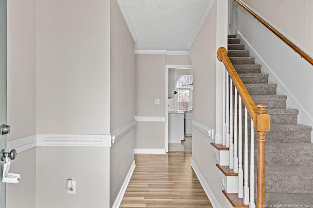 staircase with wood-type flooring, a textured ceiling, and crown molding