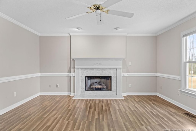 unfurnished living room with ceiling fan, a high end fireplace, crown molding, light hardwood / wood-style floors, and a textured ceiling