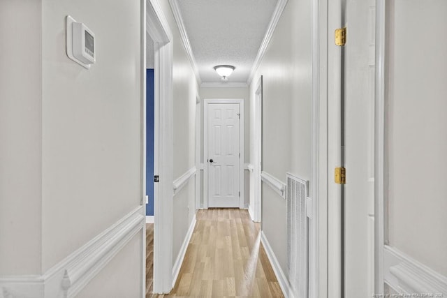 corridor with a textured ceiling, light hardwood / wood-style floors, and ornamental molding