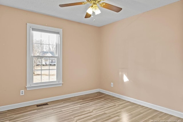 empty room with ceiling fan, plenty of natural light, light hardwood / wood-style floors, and a textured ceiling