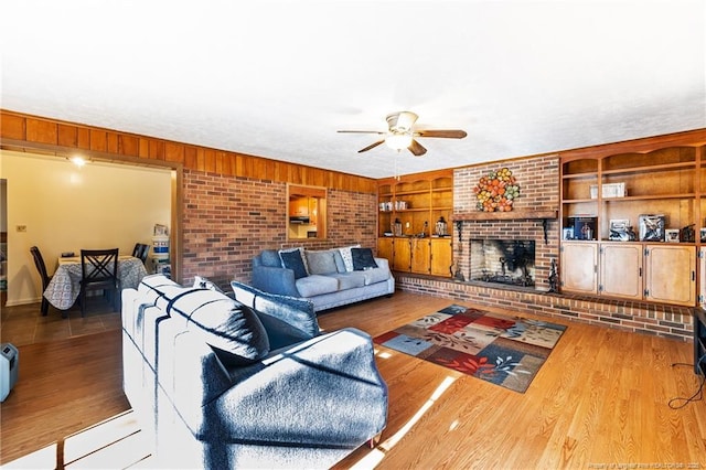 living room with ceiling fan, built in features, wood walls, a fireplace, and light wood-type flooring