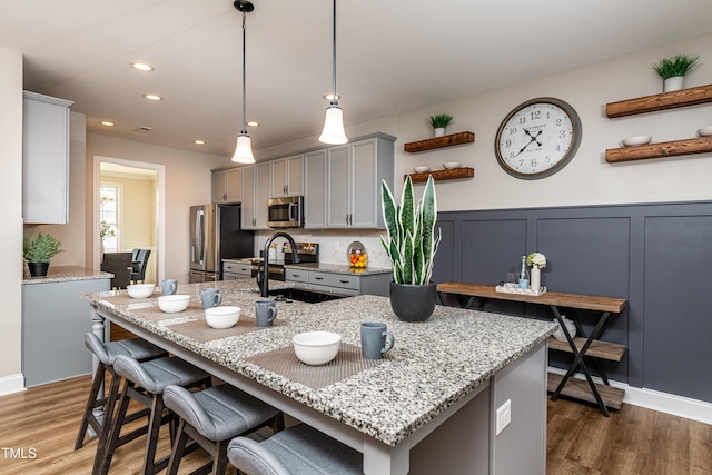 kitchen featuring appliances with stainless steel finishes, gray cabinetry, dark hardwood / wood-style flooring, hanging light fixtures, and light stone countertops