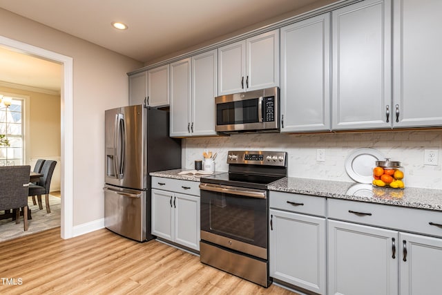 kitchen with tasteful backsplash, light stone countertops, stainless steel appliances, and light hardwood / wood-style floors