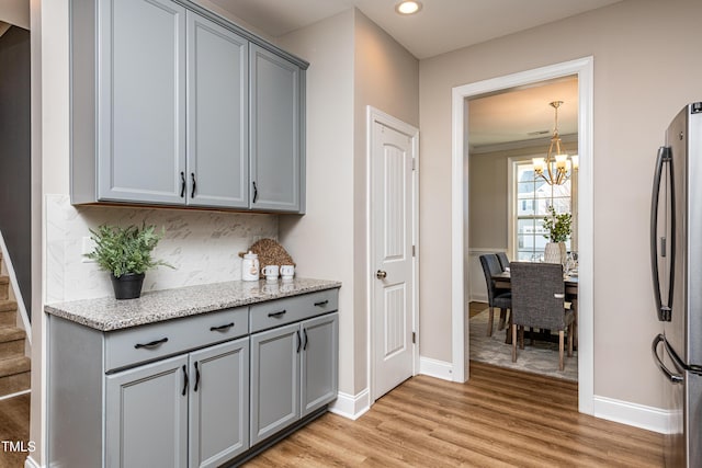 bar featuring tasteful backsplash, a notable chandelier, stainless steel refrigerator, and gray cabinetry