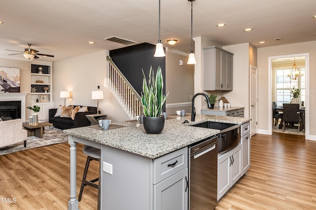 kitchen with sink, light stone countertops, a breakfast bar area, built in shelves, and ceiling fan with notable chandelier