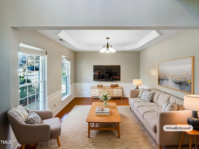 living room with a raised ceiling, wood-type flooring, and an inviting chandelier