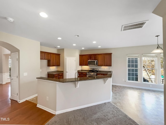 1012 Fulbright Dr, Morrisville, NC 27560 - kitchen with appliances with stainless steel finishes, arched walkways, recessed lighting, wood finished floors, and a breakfast bar