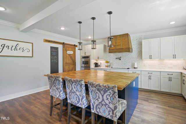 kitchen featuring a barn door, a breakfast bar, a kitchen island, white cabinetry, and pendant lighting