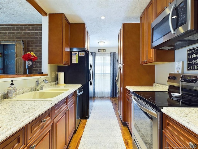 kitchen with light wood-type flooring, light stone counters, a textured ceiling, stainless steel appliances, and sink