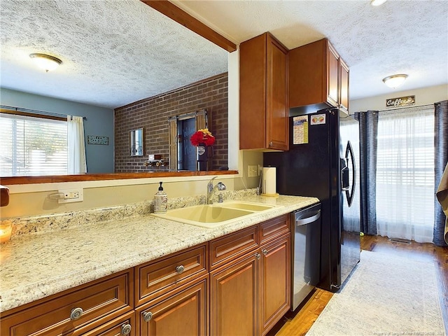 kitchen featuring a textured ceiling, light hardwood / wood-style floors, stainless steel dishwasher, and sink