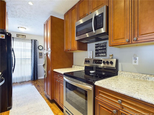 kitchen with appliances with stainless steel finishes, a textured ceiling, light hardwood / wood-style floors, and light stone counters