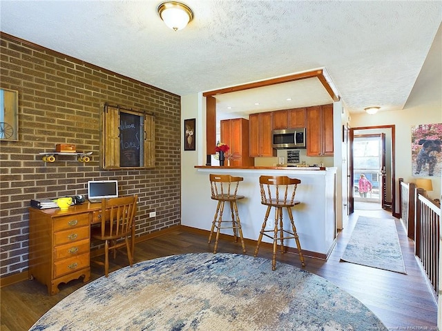 kitchen with dark wood-type flooring, brick wall, kitchen peninsula, a textured ceiling, and a kitchen bar