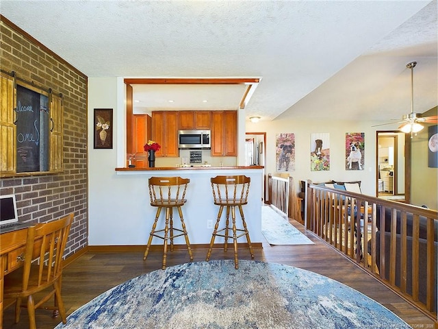 kitchen with ceiling fan, dark wood-type flooring, a kitchen breakfast bar, kitchen peninsula, and a textured ceiling