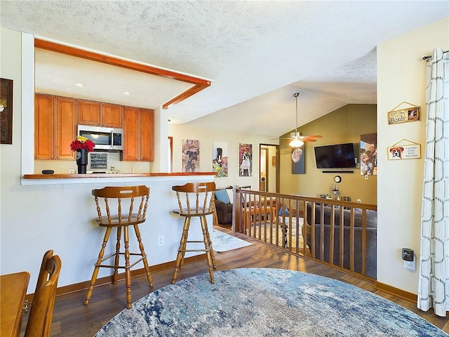 kitchen featuring a kitchen bar, kitchen peninsula, ceiling fan, and dark hardwood / wood-style floors