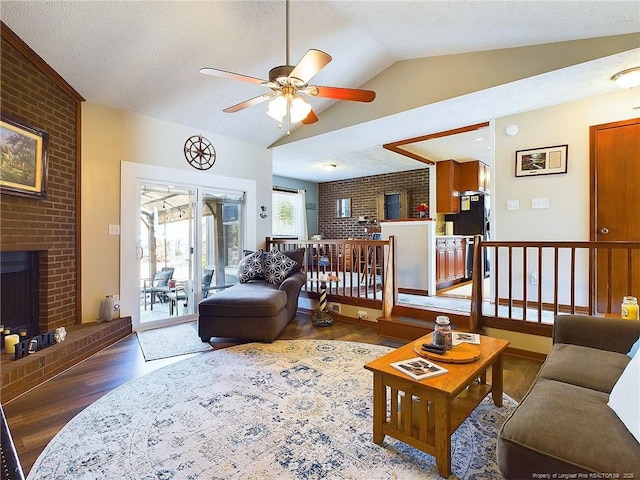 living room featuring vaulted ceiling, ceiling fan, a textured ceiling, a fireplace, and wood-type flooring