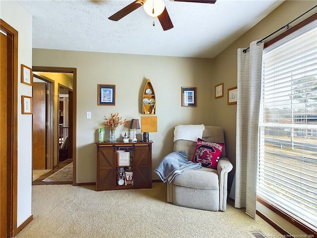 living area with ceiling fan, light colored carpet, and a textured ceiling