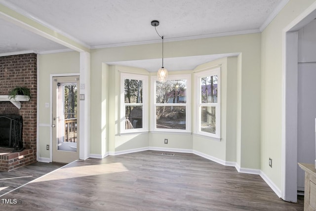 unfurnished dining area with a textured ceiling, dark hardwood / wood-style floors, a brick fireplace, and ornamental molding