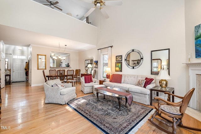 living room with ceiling fan with notable chandelier, a towering ceiling, light wood-type flooring, and a premium fireplace