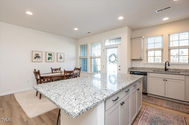 kitchen with dishwasher, light hardwood / wood-style floors, a center island, sink, and light stone countertops