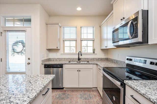 kitchen with appliances with stainless steel finishes, white cabinets, light stone counters, and sink