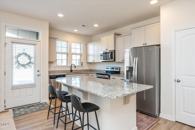 kitchen featuring stainless steel appliances, light wood-type flooring, a kitchen island, a breakfast bar, and sink