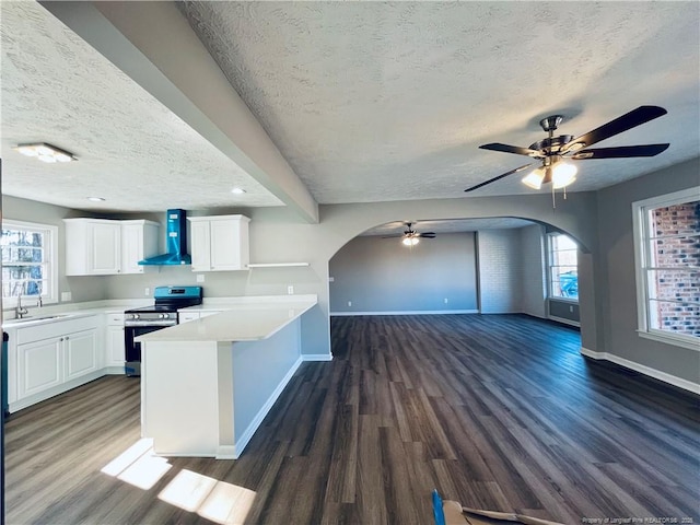 kitchen featuring dark wood-type flooring, wall chimney exhaust hood, stainless steel electric range oven, a textured ceiling, and white cabinetry